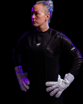 A person wearing white goalkeeper gloves with ands on hips